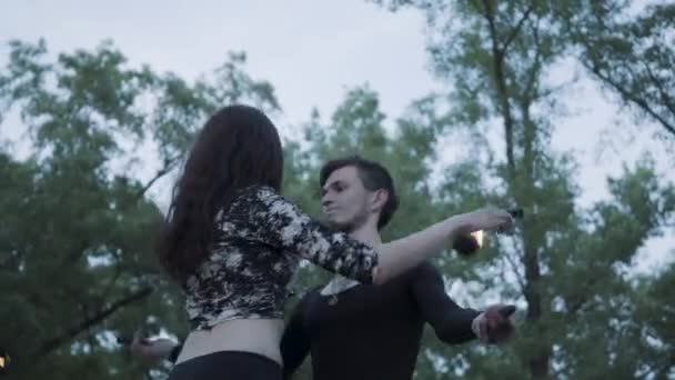 Young beautiful girl and handsome man in black clothes performing show with flame standing on the riverbank. The woman golding fireball while man exhaling powerful fiery jet over her head. Slow motion — Stock Video