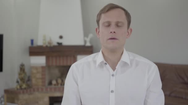 Portrait of handsome emotional blond man with amazing gray eyes in white t-shirt talking looking into the camera in the room with modern rich furniture. The guy on interview. — Stock Video