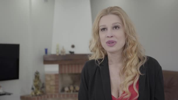 Retrato de mulher loira bonita com cabelo encaracolado em desgaste formal falando na frente da câmera na sala com mobiliário moderno. A senhora na entrevista . — Vídeo de Stock