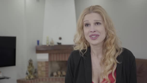 Retrato de mujer rubia linda con el pelo rizado en ropa formal hablando delante de la cámara en la habitación con muebles modernos. La dama en la entrevista . — Vídeos de Stock