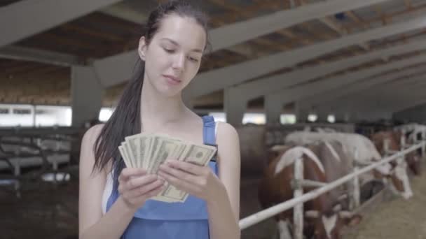 Retrato de una joven campesina linda en la granja de vacas contando dinero en efectivo. La agricultora positiva obtiene ingresos de su granja. Industria agrícola, agricultura y ganadería — Vídeos de Stock