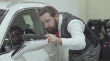 Portre çekici sevimli emin sakallı işadamı bir iş kıyafeti yeni satın oto araba bayilik inceler. Araba showroom. Reklam konsepti.