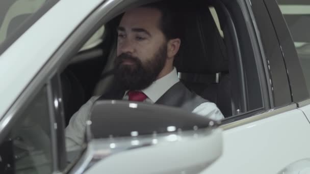 Uomo di successo seduto nell'abitacolo del nuovo veicolo ispeziona l'interno della nuova auto acquistata dalla concessionaria. Lo showroom dell'auto. Concetto pubblicitario . — Video Stock