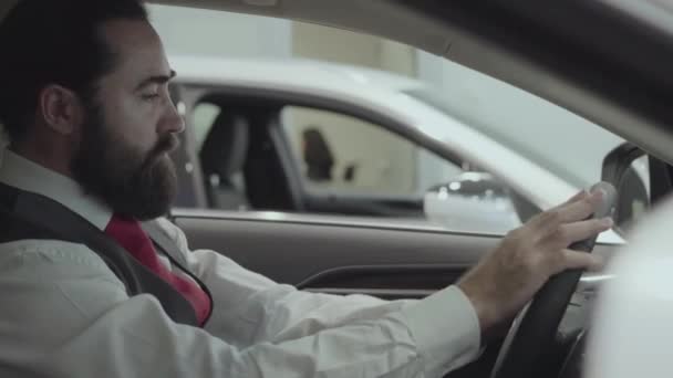 Retrato atractivo exitoso hombre de negocios barbudo sentado en el vehículo e inspecciona el automóvil recién comprado de la concesionaria de automóviles. Sala de exposición de coches. Concepto publicitario . — Vídeo de stock