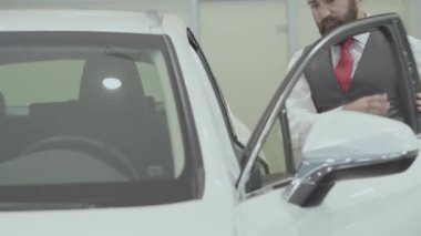 Portre çekici kendine güvenen sakallı işadamı araç oturur ve yeni otomobil Bayilik satın otomatik inceler. Araba showroom. Reklam konsepti.