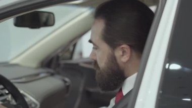 Araç içinde oturan portre çekici sevimli emin sakallı işadamı ve araç Bayilik yeni satın otomatik inceler. Araba showroom. Reklam konsepti.