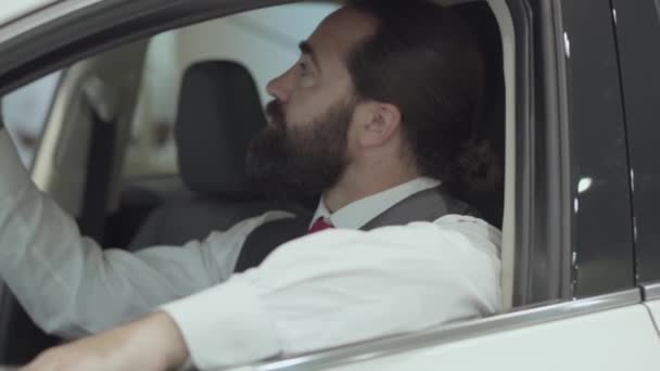 Ritratto attraente uomo d'affari barbuto sicuro seduto nel veicolo e ispeziona auto appena acquistata dalla concessionaria auto. Lo showroom dell'auto. Concetto pubblicitario . — Video Stock