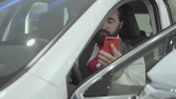 Portrait attrayant homme d'affaires barbu confiant assis dans le véhicule et inspecte l'automobile nouvellement acheté auprès du concessionnaire automobile. Homme qui parle avec succès par téléphone portable tout en étant assis dans une voiture . — Video