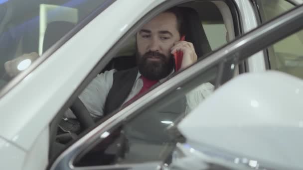 Portret aantrekkelijke vertrouwen baard zakenman zitten in het voertuig en inspecteert nieuw aangekochte auto van de auto dealer. Succesvolle man praten door mobiele telefoon zittend in een auto. — Stockvideo