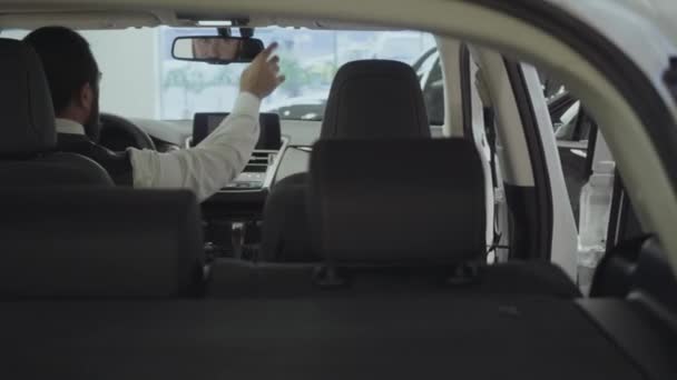 Porträtt attraktiv säker skäggiga affärs man sitter i fordonet och inspekterar nyinköpt bil från bil handlaren. Bil showroom. Reklam koncept. — Stockvideo