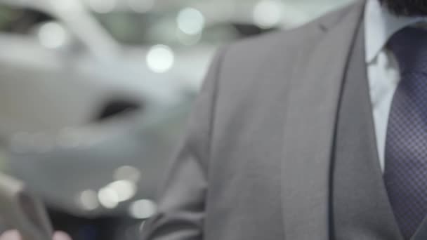 Unrecognized successful business man in a business suit showing the key of a luxury car looking into the camera. Car showroom. Advertising concept. — Stock Video