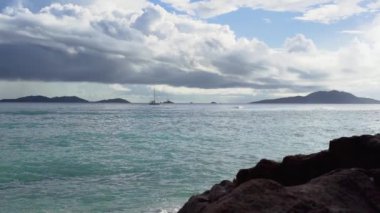 Seyşeller. Praslin Adası. Kumlu plajda köpüklü dalgalar rulo. Taşlar ön planda. Yavaş hareket.