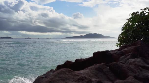 Seicheles. Ilha Praslin. Ondas espumosas rolam na praia de areia. Pedras em primeiro plano. Movimento lento . — Vídeo de Stock