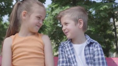 Sevimli sarışın erkek ve güzel kız oyun üzerinde salıncak üzerinde oturan Portresi. Birkaç mutlu çocuk. Açık havada aşık komik çocuklar.