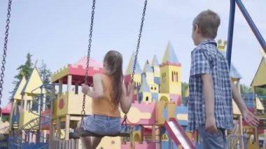 Sevimli çocuk uzun saçlı güzel bir kız salıncak üzerinde sallanan, gülümseyerek. Birkaç mutlu çocuk. Aşık komik kaygısız çocuklar açık havada.