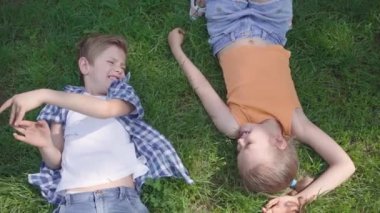 Portre iki eğlenceli sevimli sevimli çocuklar parkta birbirlerine gülümseyerek çim üzerinde yatan. Komik kız oğlanın elini eline alıyor. Birkaç mutlu çocuk. Aşık komik kaygısız çocuklar. Üstte görüntü