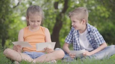 Parkta uzun saçlı sevimli yakışıklı erkek ve güzel kız Portresi fotoğraflar aranıyor. Yaz eğlencesi açık havada. Sevimli çocuklar ağaçların altında eğlenirler.