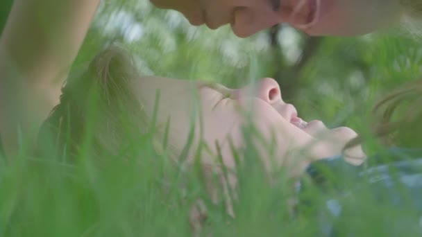 Крупним планом портрет милої маленької дівчинки, яка цілує лоб і ніс хлопчика, що лежить в траві. Кілька щасливих дітей. Веселі безтурботні діти в любові — стокове відео