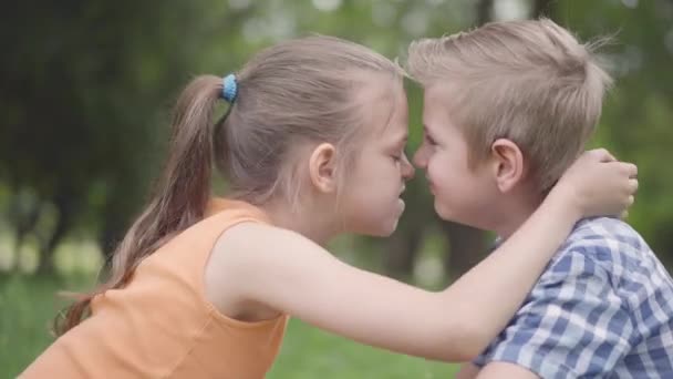 귀여운 소년과 소녀의 측면보기는 공원에 앉아, 자신의 코를 문질러 재미. 행복한 아이들 몇 명. 재미 평온한 아이 에 사랑 — 비디오