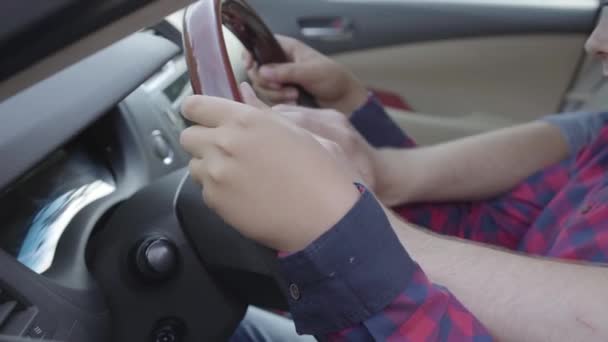 Невпізнаваний молодий батько навчає свого сина водити машину крупним планом. Хлопчик сидить на батьківських кільцях, обидва кладуть руки на кермо. Дитина і батько проводять час разом — стокове відео