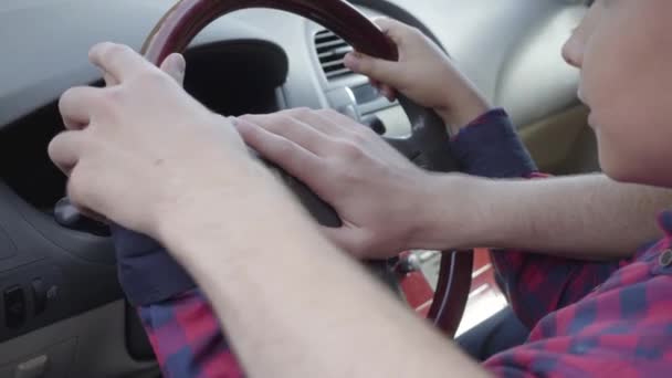 Un jeune père méconnaissable apprenant à son fils à conduire la voiture de près. Le garçon assis sur des tours de pères, les deux mains sur le volant. L'enfant et le père passent du temps ensemble — Video