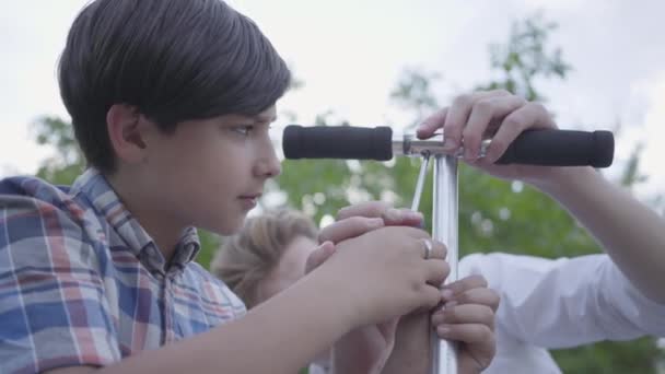 Young father teaching his son to fix scooter close-up. Side view of cute boy with screw driver, trying to unscrew the screw. A man passes on knowledge to a son — ストック動画