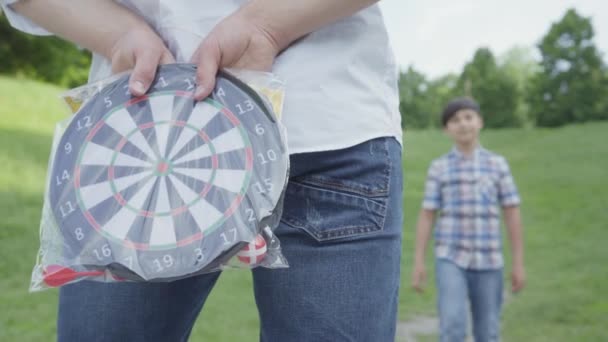 Nierozpoznawalny ojciec ukrywa rzutki za powrotem stojący z powrotem do kamery na pierwszym planie. Cute Boy na tle najbliższych i biorąc prezent. Człowiek ma prezent dla dziecka — Wideo stockowe