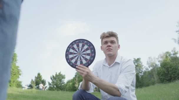 Neşeli genç baba, oğlu dairelerde bir mıknatıs üzerinde dart atarken dart tutan. Aile eğlencesi açık havada. Baba ve bir çocuk dışarıda birlikte vakit geçirirler. Baba çocuğunu destekliyor. — Stok video