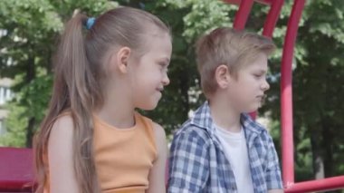 Sevimli erkek ve kız parkta yakın salıncak ta oturan, hassasiyetle birbirlerine bakıyor. Birkaç mutlu çocuk. Aşık komik çocuklar