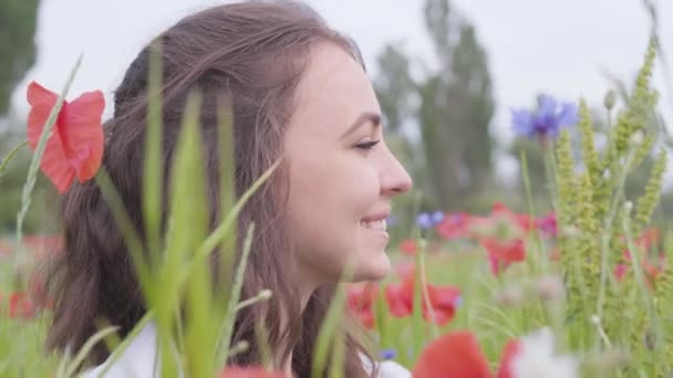 Close-up portret schattig meisje zittend in Poppy veld. Schattig gelukkig glimlachend meisje rust buitenshuis. Contrasterende kleuren in Poppy. Bloeiende klaprozen. Liefde natuur concept. Vrije tijd in de natuur. — Stockvideo