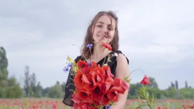 Portre sevimli genç kadın elinde bir haşhaş alanında duran kameraya bakarak çiçek bukettutan. Doğayla bağlantı. Yeşil ve kırmızı uyum. Doğada eğlence.