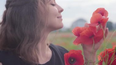 Portre sevimli genç kadın elinde bir haşhaş alanında duran kameraya bakarak çiçek bukettutan. Doğayla bağlantı. Yeşil ve kırmızı uyum. Doğada eğlence.