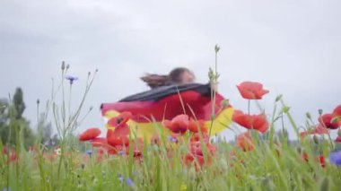 Açık havada elinde Almanya bayrağı tutan bir haşhaş tarlasında dans sevimli genç kız. Doğayla bağlantı, vatanseverlik. Doğada boş zaman. Çiçek açan haşhaşlar. Özgürlük.