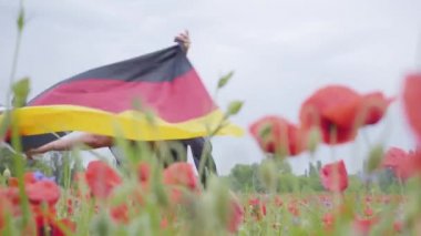 Sevimli sevimli genç kız elinde açık havada Almanya bayrağı tutan bir haşhaş alanında dans. Doğayla bağlantı, vatanseverlik. Doğada boş zaman. Çiçek açan haşhaşlar. Özgürlük.