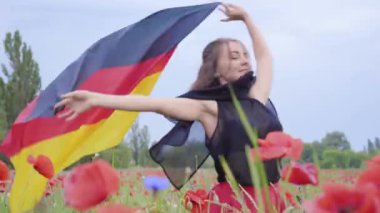 Açık havada elinde Almanya bayrağı tutan bir haşhaş alanında dans sevimli sevimli genç kadın. Doğayla bağlantı, vatanseverlik. Doğada boş zaman. Çiçek açan haşhaşlar. Özgürlük.
