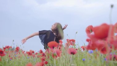 Haşhaş tarlasında mutlu bir şekilde gülümseyen güzel bir kız. Doğayla bağlantı. Doğada boş zaman. Çiçek açan haşhaşlar. Özgürlük.