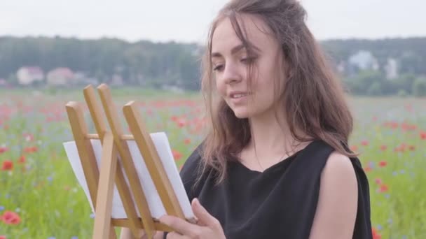 양귀비 필드에 이젤 에 그림 귀여운 밀링 소녀의 초상화. 야외에서 젊은 여성 예술가. 자연과의 연결. 사랑의 자연 개념. — 비디오