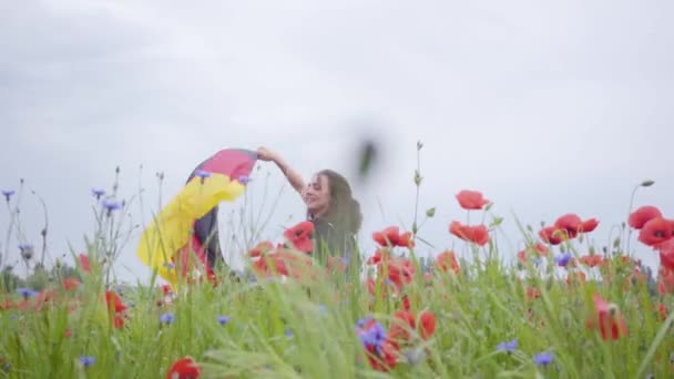 Açık havada elinde Almanya bayrağı tutan haşhaş tarlasında dans eden güzel bir kız. Doğayla bağlantı, vatanseverlik. Doğada boş zaman. Çiçek açan haşhaşlar. Özgürlük. — Stok video