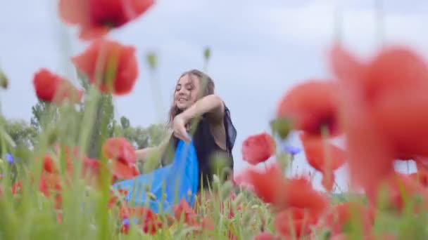 肖像可爱的可爱的年轻女子在罂粟地跳舞，手里拿着乌克兰国旗在户外。与自然的联系，爱国主义。大自然中的休闲。开花的罂粟。自由. — 图库视频影像