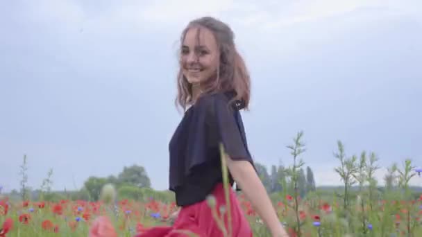 Mooie jonge vrouw rennen en dansen in een klaproos veld glimlachend gelukkig. Verbinding met de natuur. Vrije tijd in de natuur. Bloeiende klaprozen. Vrijheid. — Stockvideo