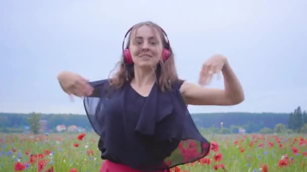 Όμορφη νέα γυναίκα φορώντας ακουστικά ακούγοντας μουσική και χορεύοντας σε ένα πεδίο παπαρούνας χαμογελαστή ευτυχισμένη. Σύνδεση με τη φύση. Αναψυχή στη φύση. Παπαρούνες που ανθίζουν. Ελευθερία. — Αρχείο Βίντεο
