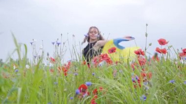 Sevimli sevimli genç kadın elinde açık havada Ukrayna bayrağı tutan bir haşhaş alanında dans. Doğayla bağlantı, vatanseverlik. Doğada boş zaman. Çiçek açan haşhaşlar. Özgürlük.