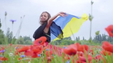 Portre sevimli genç kadın elinde açık havada Ukrayna bayrağı tutan bir haşhaş alanında dans. Doğayla bağlantı, vatanseverlik. Doğada boş zaman. Çiçek açan haşhaşlar. Özgürlük.