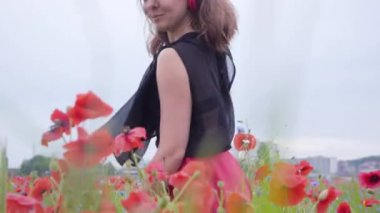 Kulaklık takan güzel genç kadın müzik dinliyor ve bir haşhaş tarlasında mutlu bir şekilde gülümsüyor. Doğayla bağlantı. Doğada boş zaman. Çiçek açan haşhaşlar. Özgürlük.