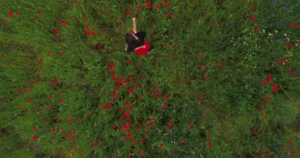 Vista desde arriba de una hermosa joven con auriculares escuchando música y bailando en un campo de amapola sonriendo felizmente. Conexión con la naturaleza. Ocio en la naturaleza. Amapolas florecientes. Disparos con drones . — Vídeos de Stock