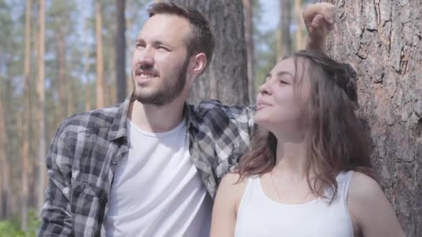 Portrait of handsome young man and pretty woman looking away, pointing with fingers up in the pine forest. Unity with wild nature. The couple resting outdoors — Stock Video