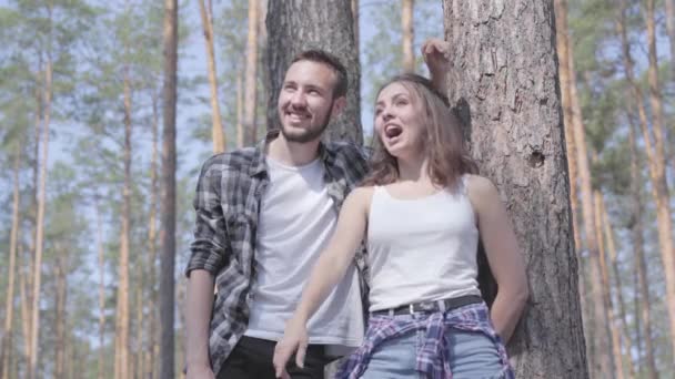 Retrato de un joven guapo y una mujer guapa mirando hacia otro lado en el bosque de pinos. Concepto de camping. Ocio y viaje a la naturaleza. Linda pareja al aire libre . — Vídeo de stock