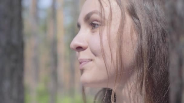 Крупним планом портрет щасливої усміхненої молодої жінки, яка дивиться навколо в сосновому лісі. Концепція кемпінгу. Дозвілля і подорож до природи . — стокове відео