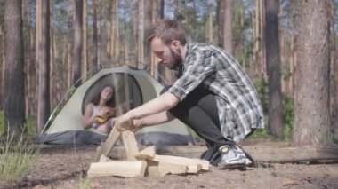 Genç adam ormanda ön planda ateş yakıyor, genç kadın ise çadırın arka planında ukulele oynuyor. Sevgi dolu bir çift dışarıda dinleniyor. Doğa ile birlik