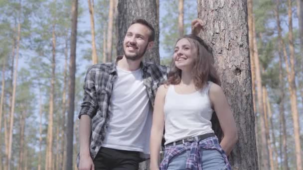 Retrato de un joven guapo y una mujer guapa mirando hacia otro lado en el bosque de pinos. Concepto de camping. Ocio y viaje a la naturaleza. Linda pareja al aire libre . — Vídeo de stock